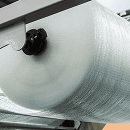 A roll of clear bubble packaging material mounted on a converting machine, the bubbles catching the light.