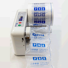An X AIR air pillow machine with a chain of inflated PBE-printed air pillows running out of it onto the bench.